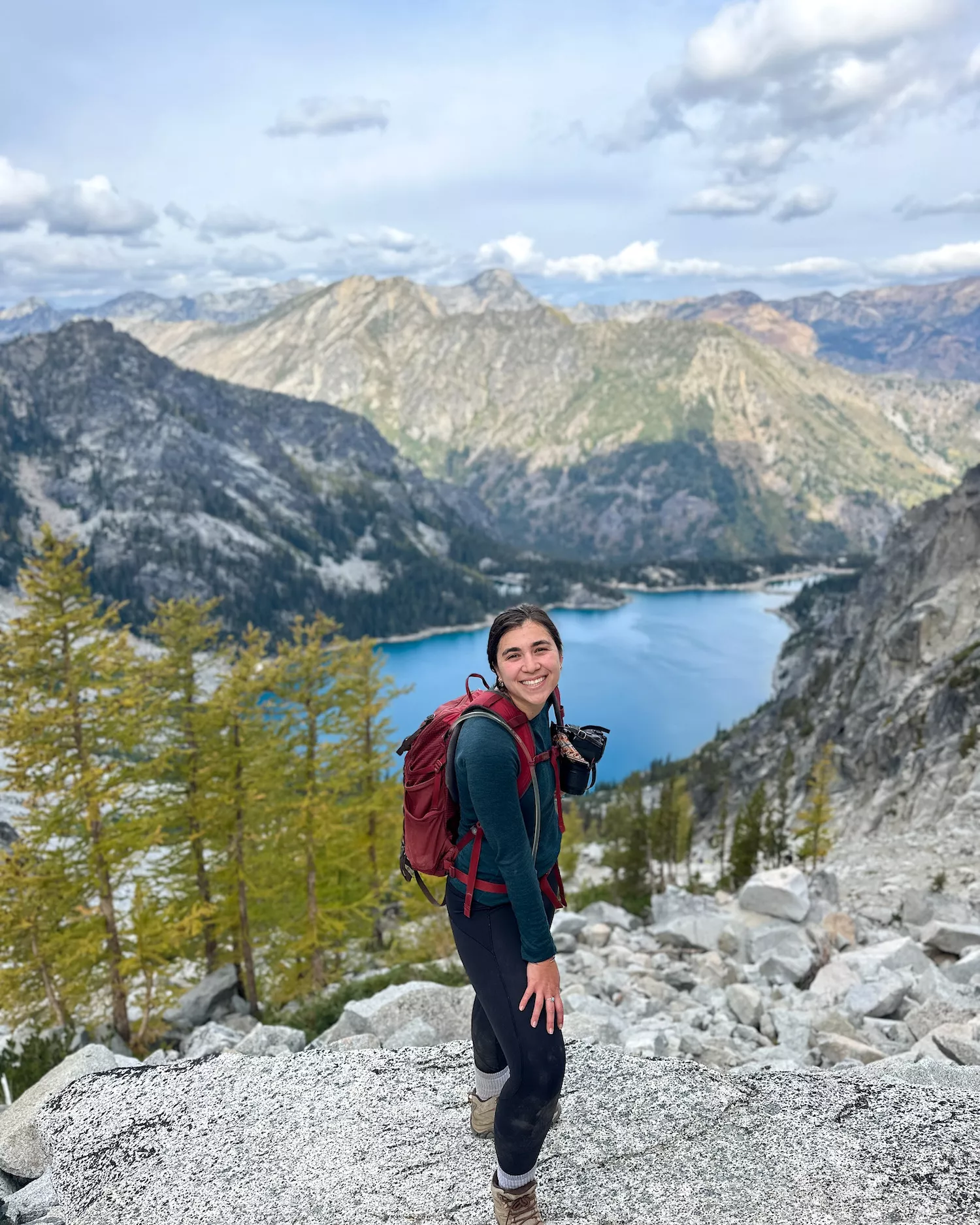girl smiling at the top of a mountain pass with blue lake below her; enchantments aasgard pass