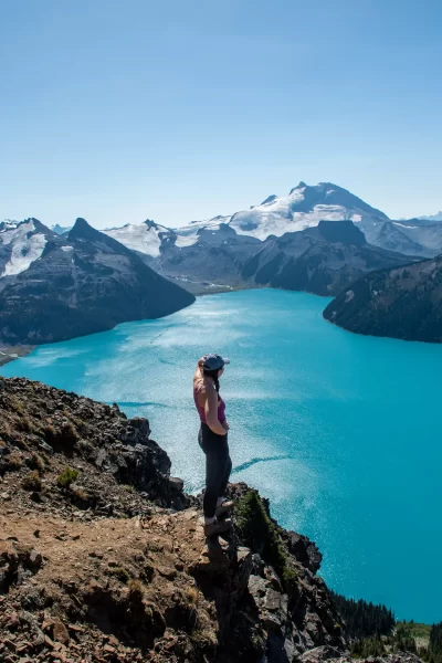 girl looking out over bright blue Garibaldi Lake with mountains above