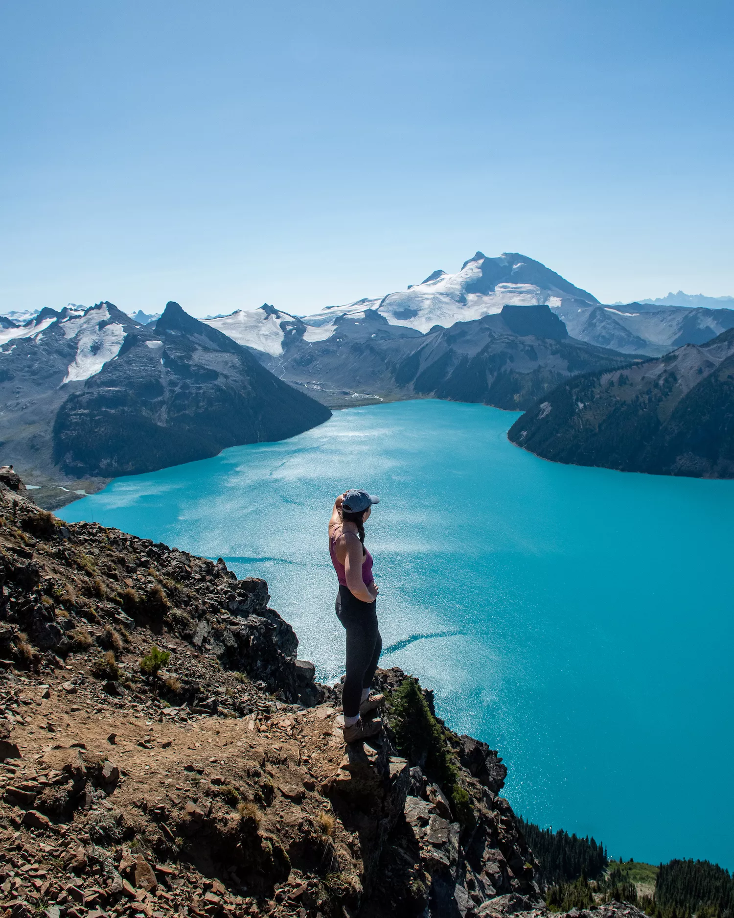 girl looking out over bright blue Garibaldi Lake with mountains above