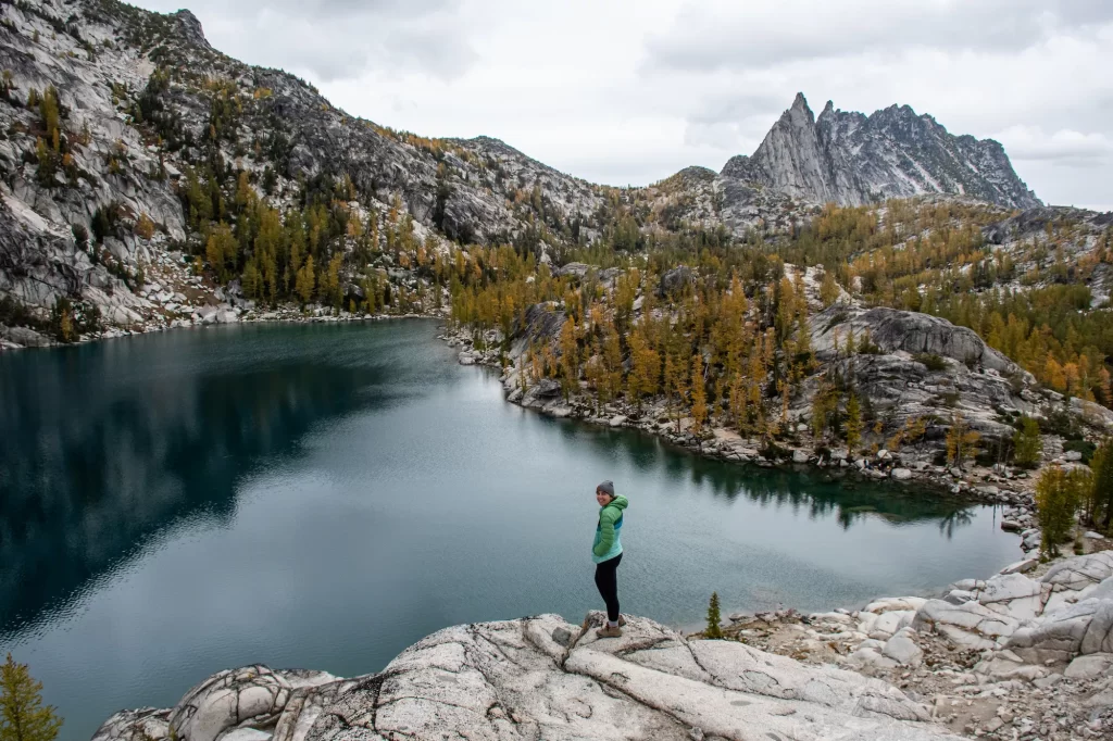 The Enchantments, girl standing on a rock above a deep blue Inspiration lake with larches behind her