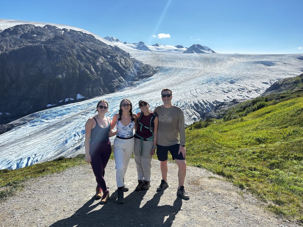 four people standing in front of exit glacier on a sunny day