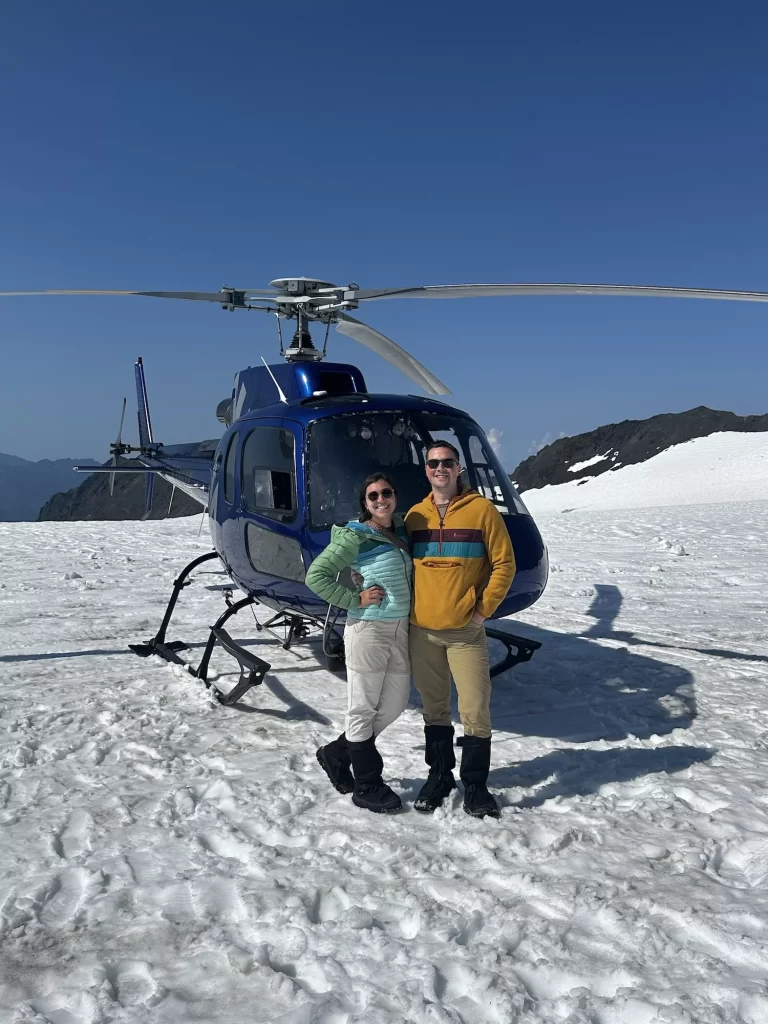 two people on a glacier in front of a helicopter