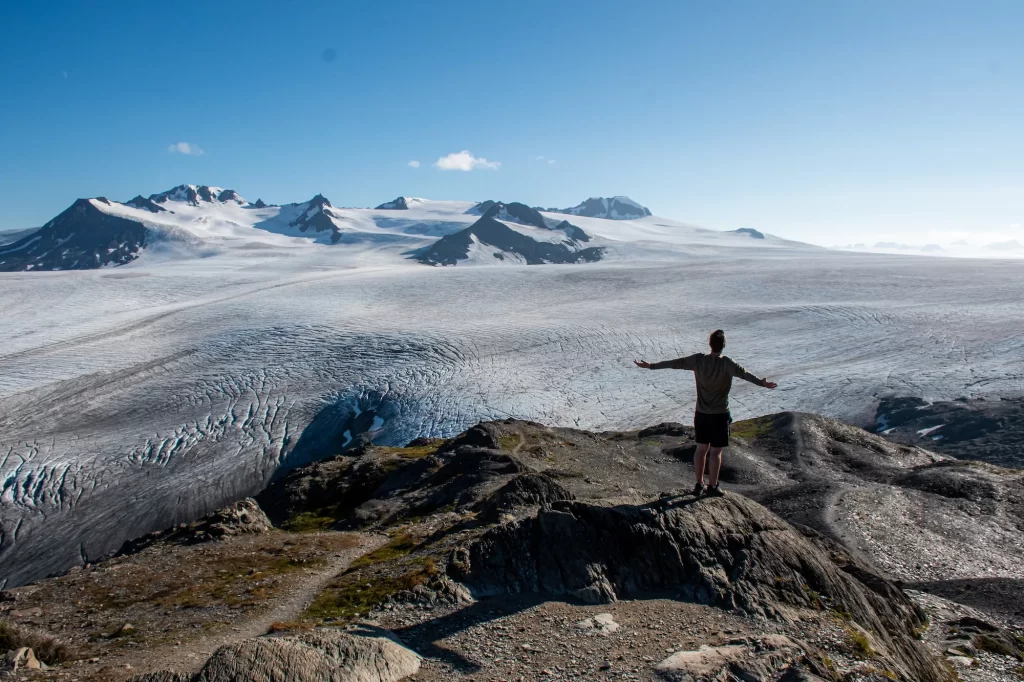 guy standing on top of harding icefield summit with arms out