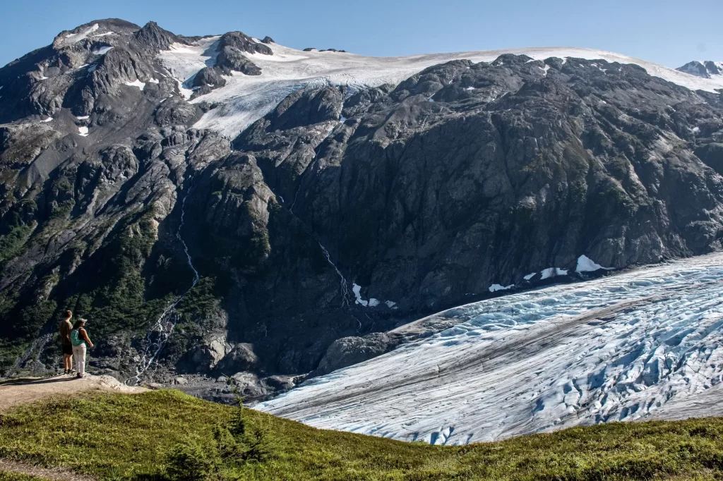 two people standing on a cliff side with glacier behind