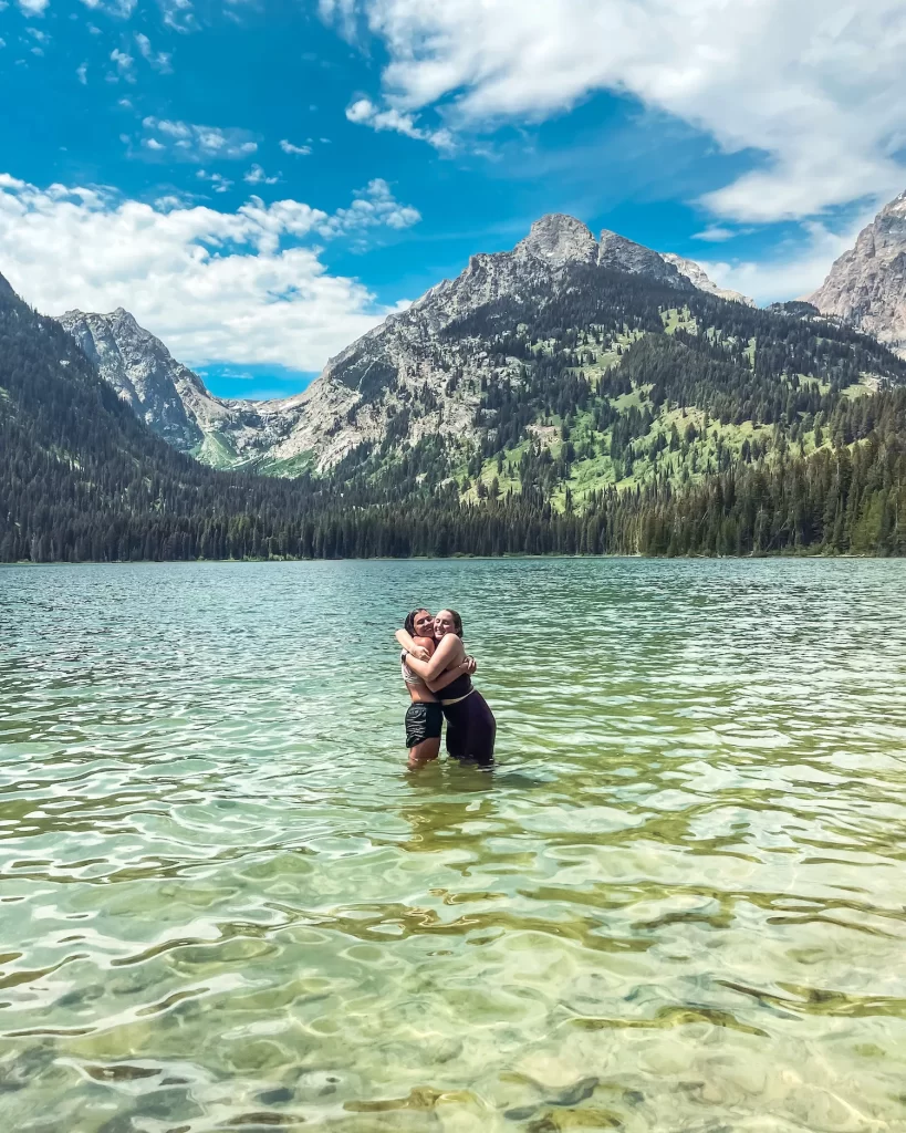 two girls hugging in a lake with tetons behind
