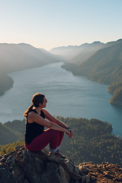 Girl sitting on top of ledge in Mount Storm King with water below and mountains