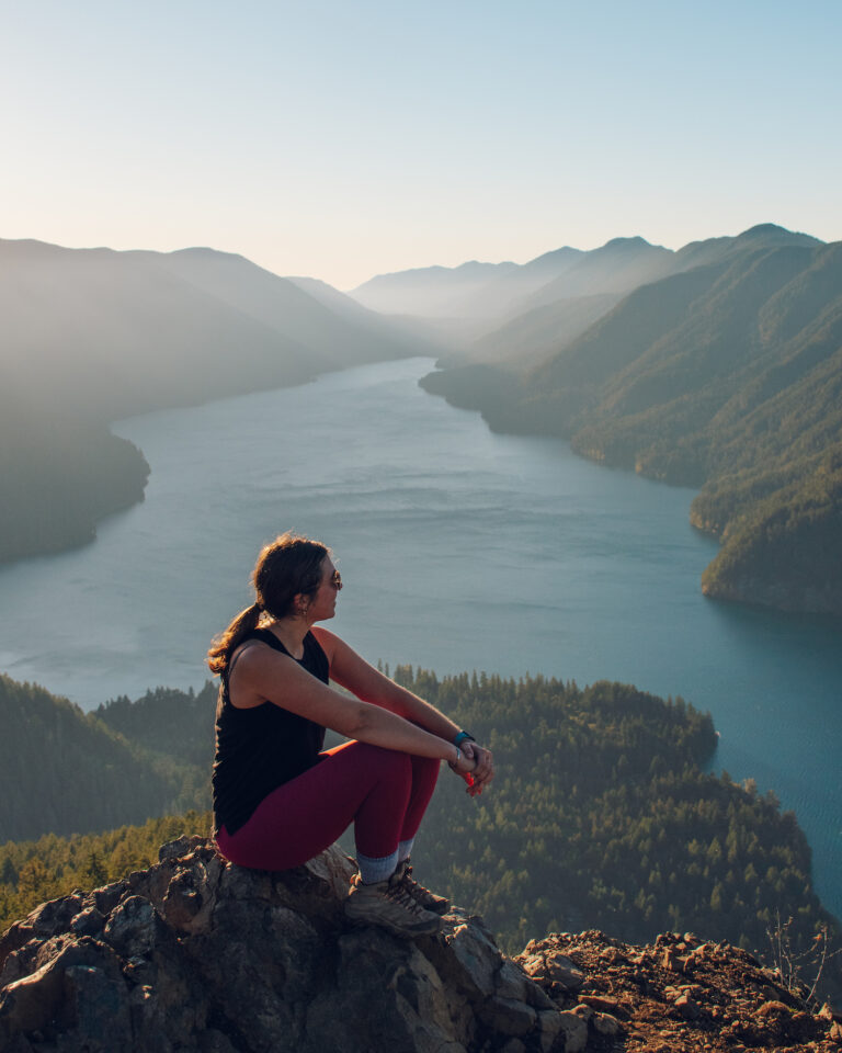 Girl sitting on top of ledge in Mount Storm King with water below and mountains
