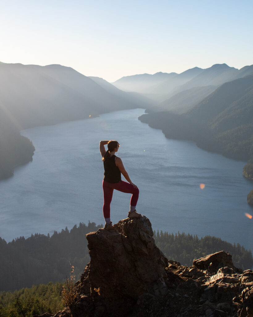 girl standing on a rock on mountain summit over water with mountains