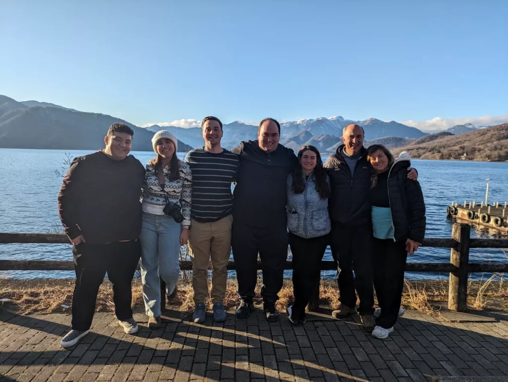 7 people smiling and posing in front of a lake