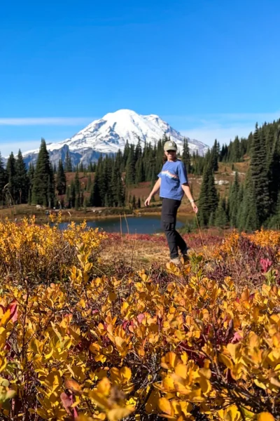 girl standing in front of mount rainier as yellows and reds cover the ground