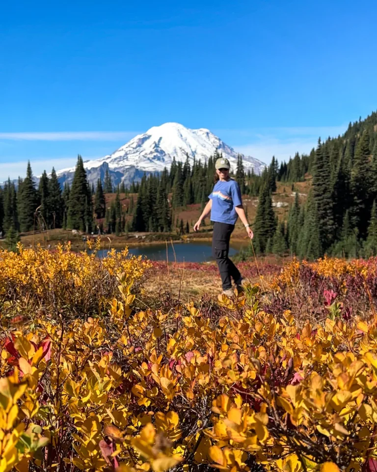 girl standing in front of mount rainier as yellows and reds cover the ground