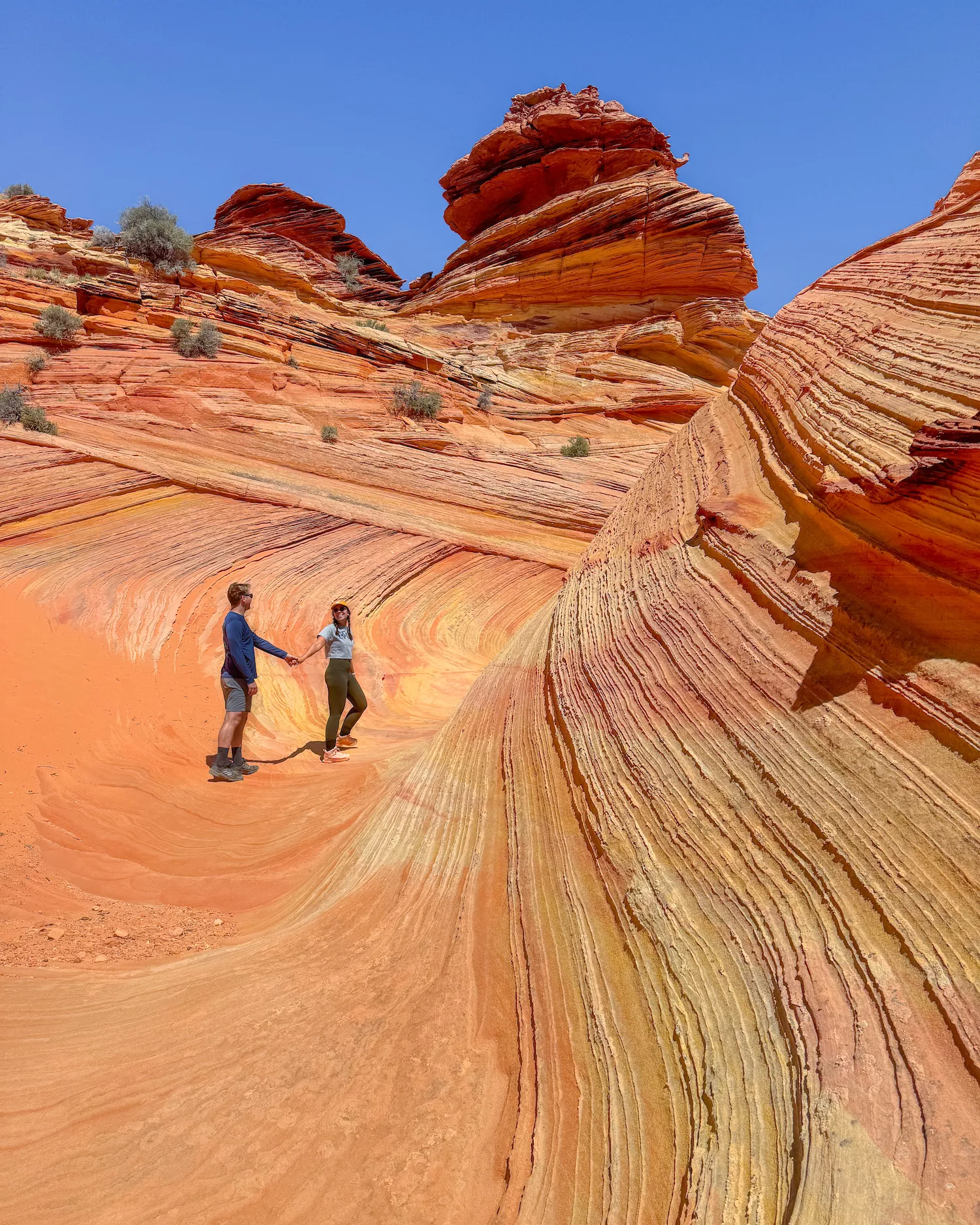 girl and boy holding hands and walking along wave like sandstone formation
