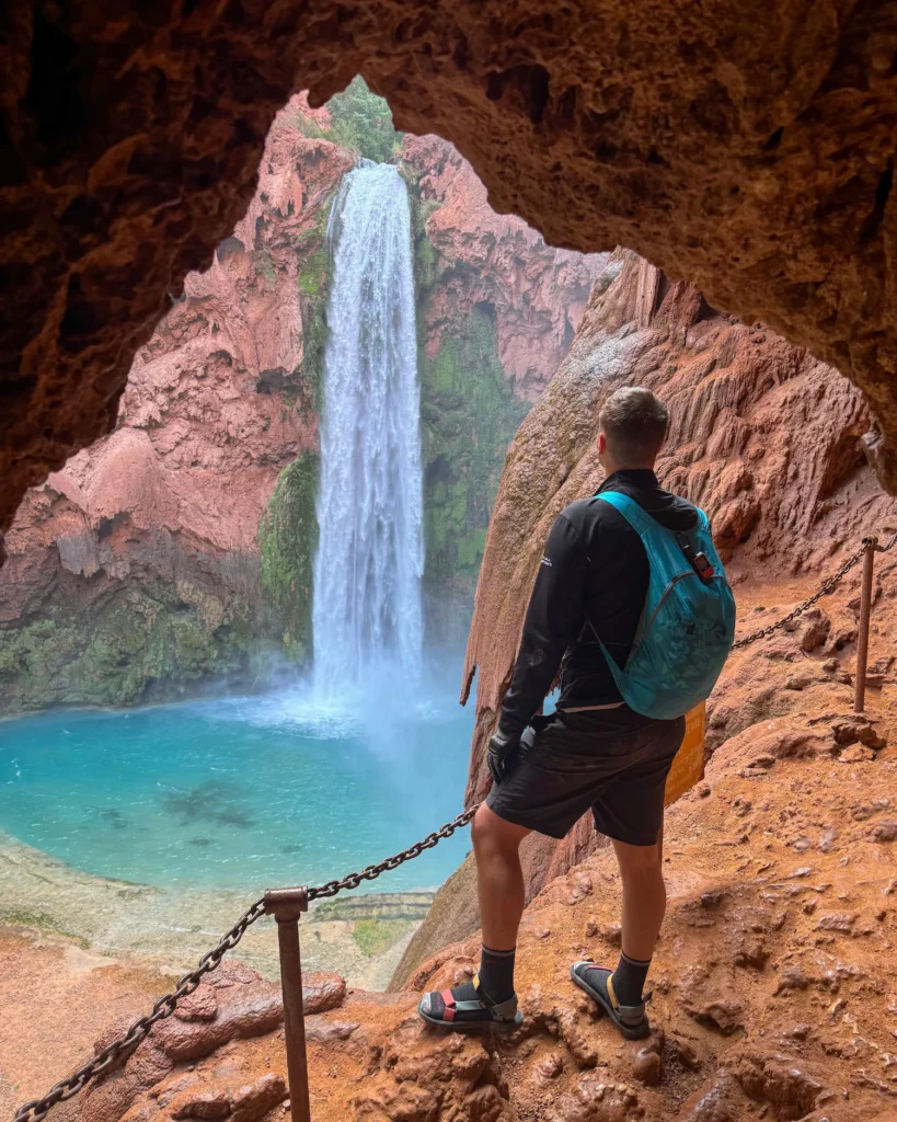 guy standing in a cave with mooney falls behind him