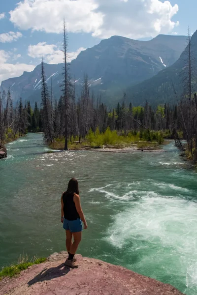girl standing on rock overlooking river with mountains in the back at glacier in May
