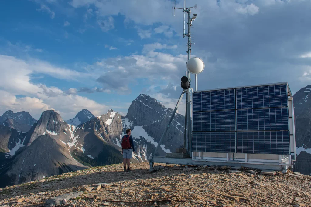 guy standing next to weather station with mountains behind
