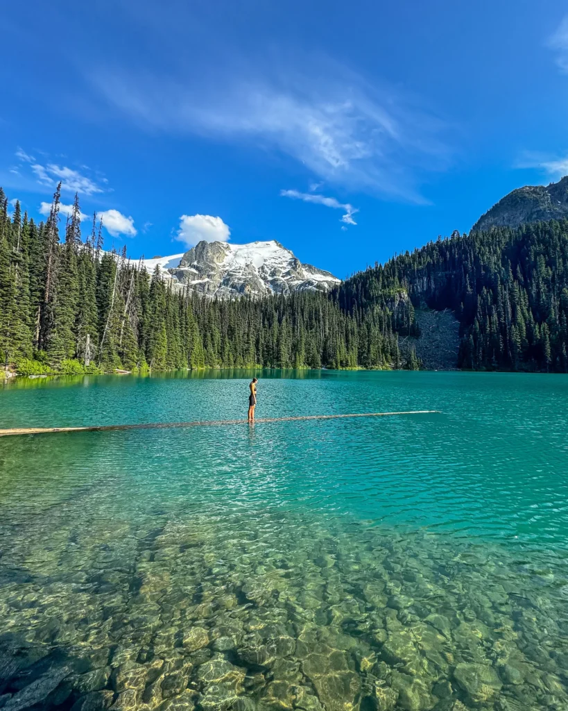 Girl standing on a log in gorgeous colored joffre lakes