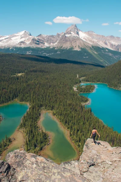 girl standing on Opabin Prospect, which is a view point over Lake O'Hara area with three lakes and mountains in the back