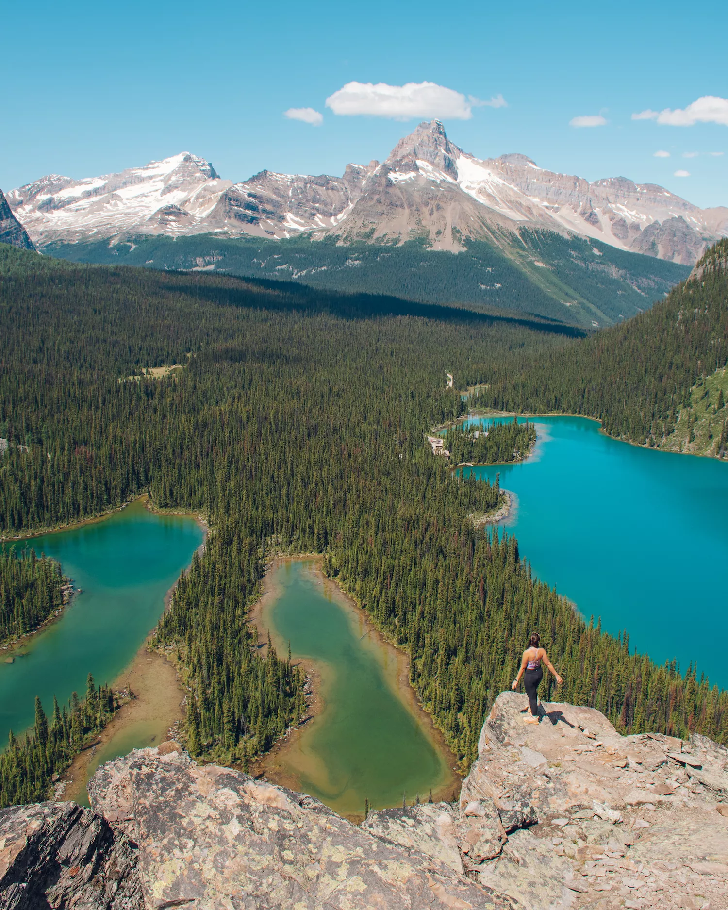 girl standing on Opabin Prospect, which is a view point over Lake O'Hara area with three lakes and mountains in the back
