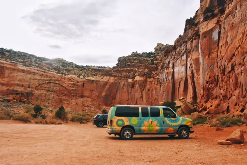 Campervan with flowers on it in Capitol Reef with red rocks above it