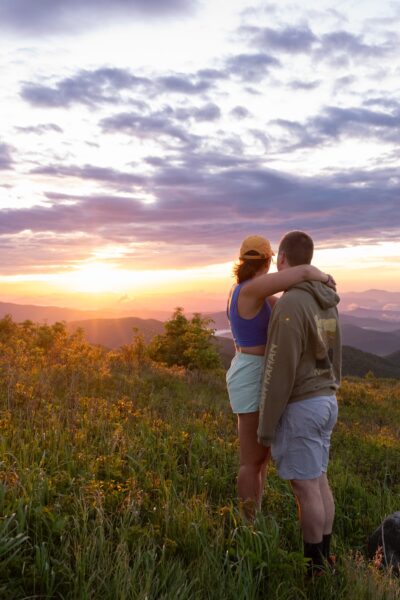 Couple looking out over sunrise at Black Balsam Knob with wildflowers blooming next to them