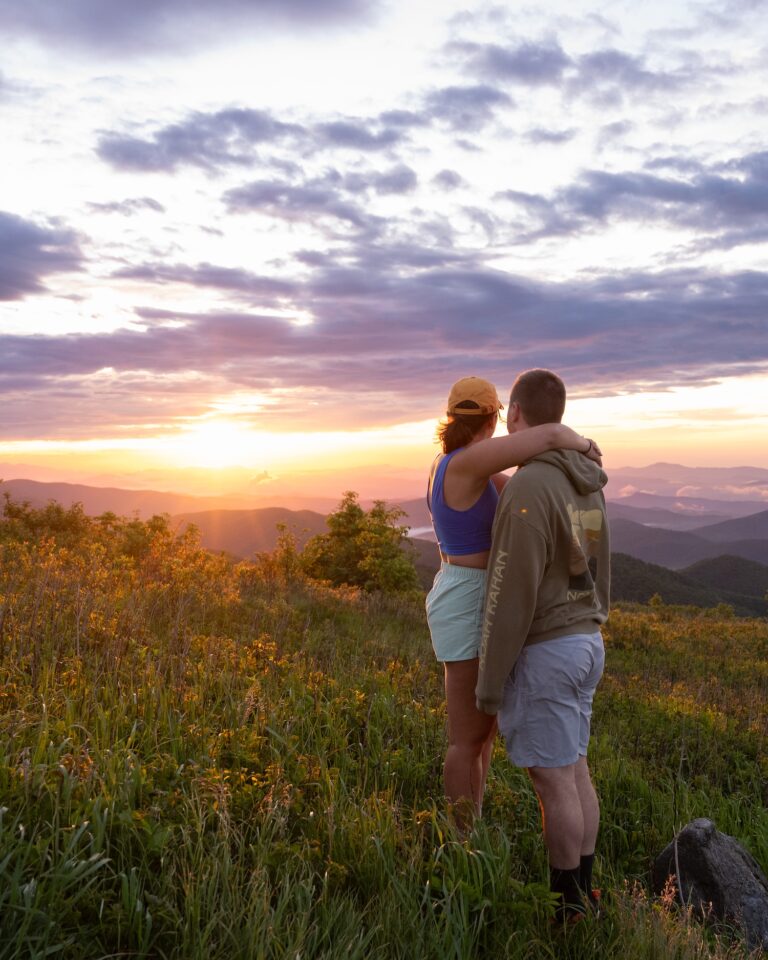 Couple looking out over sunrise at Black Balsam Knob with wildflowers blooming next to them