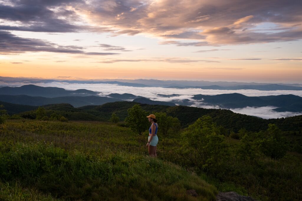 girl standing on middle of black balsam knob with mountain scapes behind her
