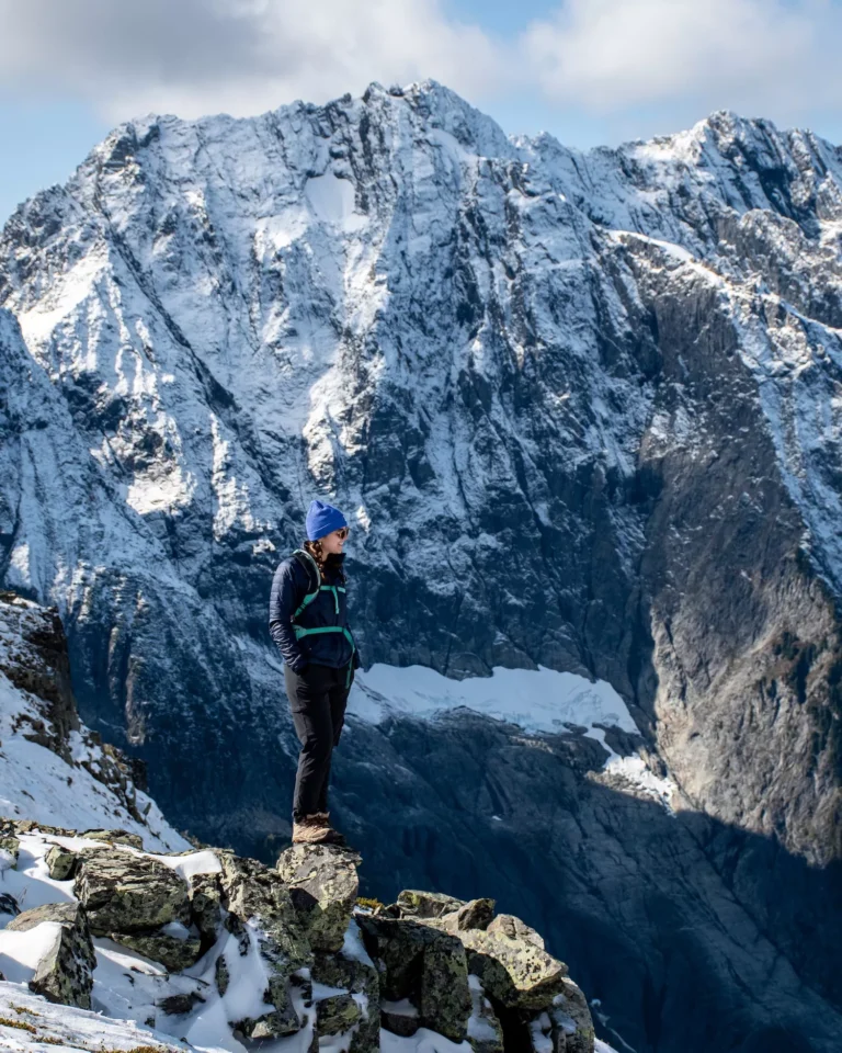 Woman standing and smiling at the top of Sahale Arm on Cascade Pass trail with snowy mountain behind her