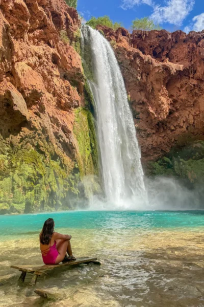 Girl looking at Mooney Falls, sitting on a table with turquoise waters