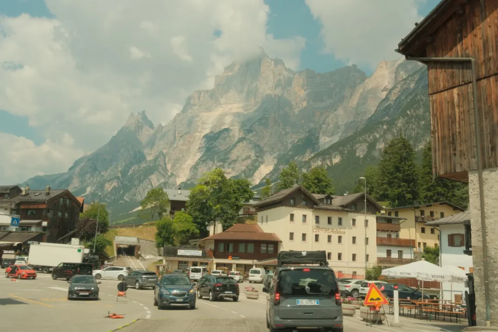 Drive through dolomites with the mountains overhead and small charming buildings below