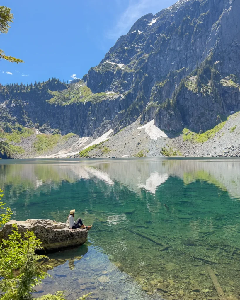 girl sitting on a rock in Lake Serene, looking up at Mount Index
