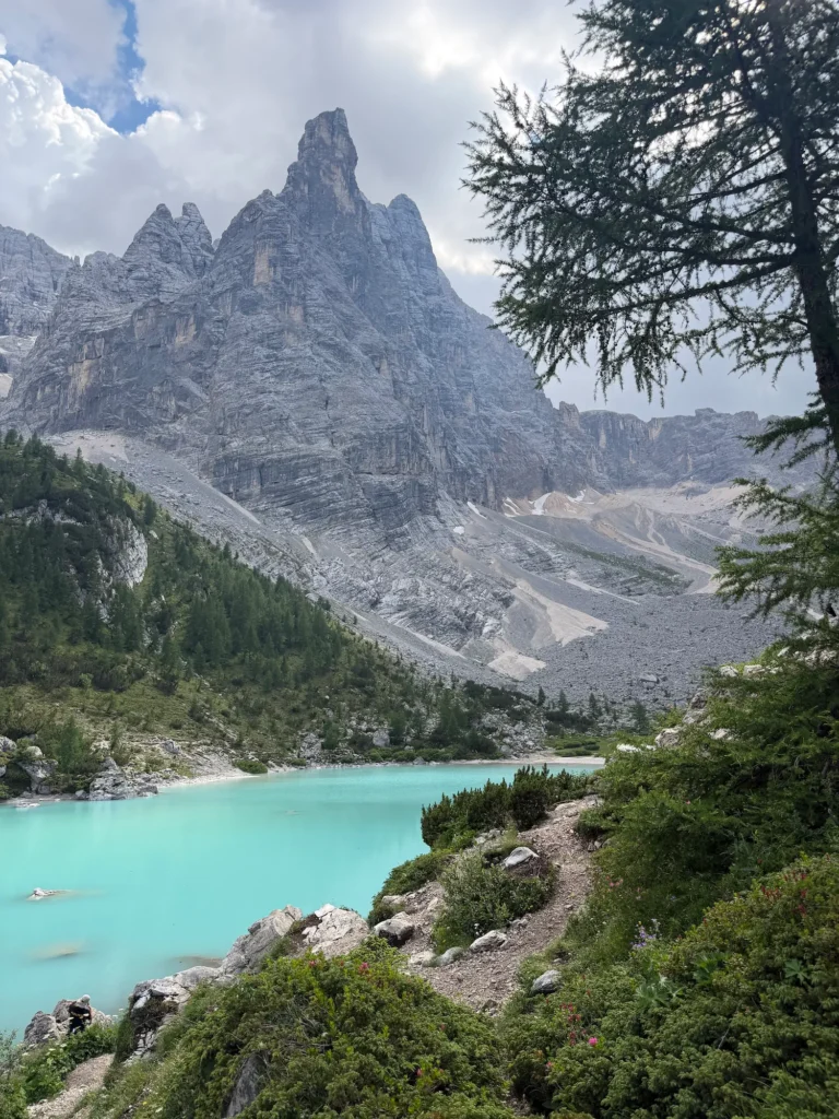 trail leading up to the icy blue Lake Sorapis with tall peak over it