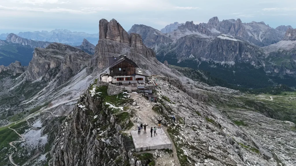 people standing in front of rifugio nuvolau and a drone shot of the surrounding area